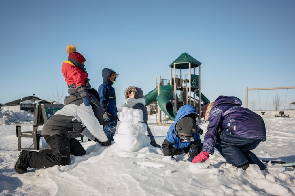 A family building a snowman near a playground