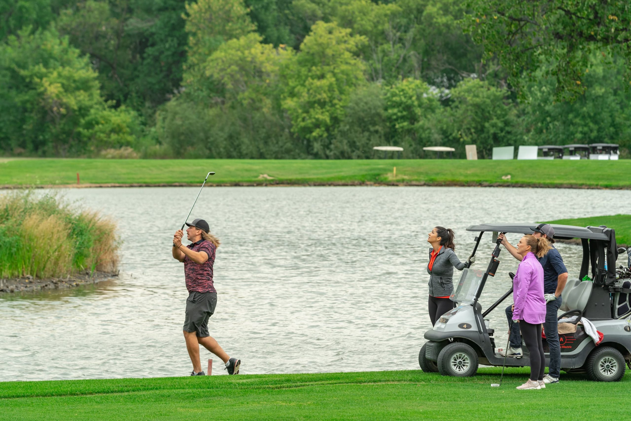 a golfer swings while friends look on