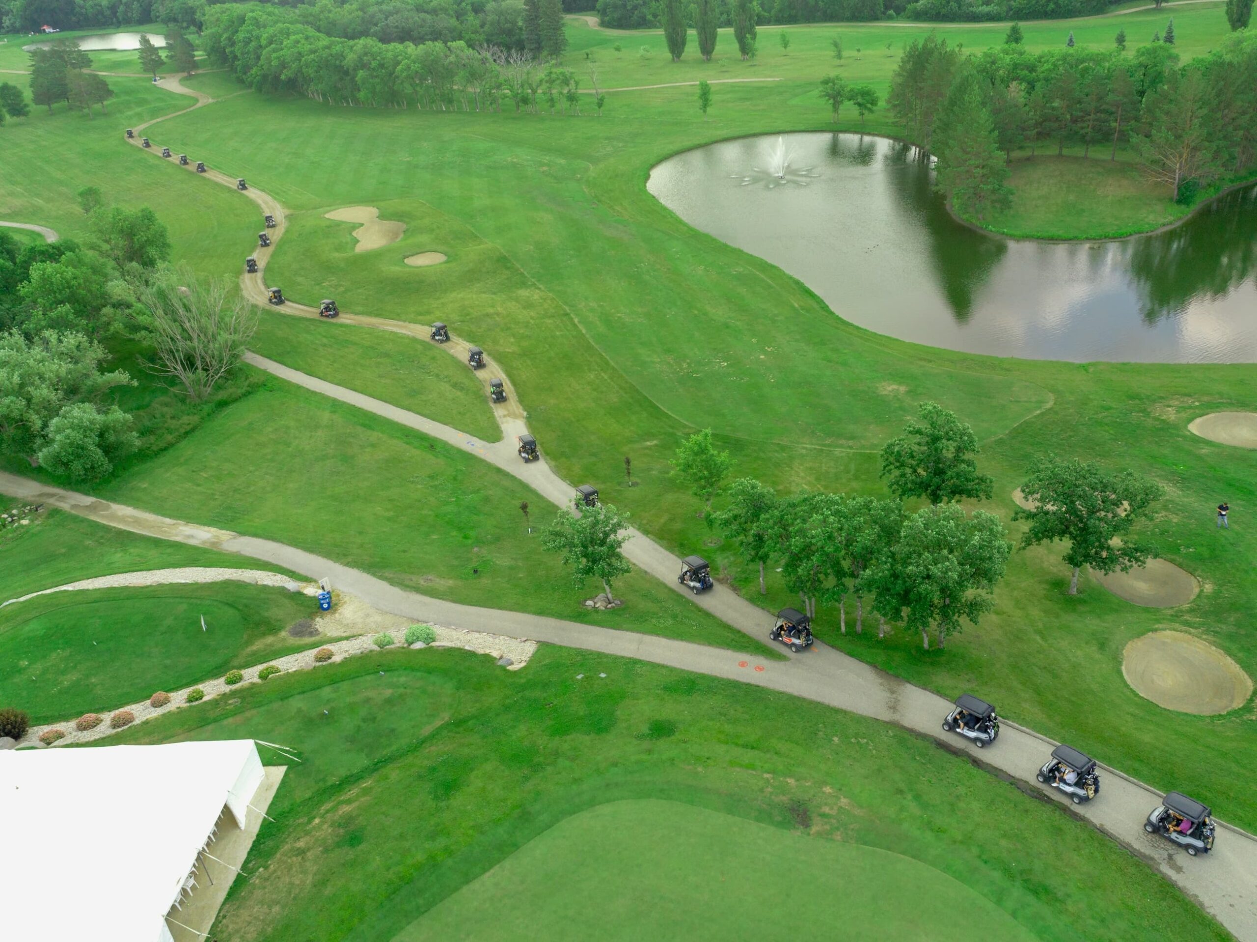 Aerial view of a row of golf carts driving down the path beside a pond